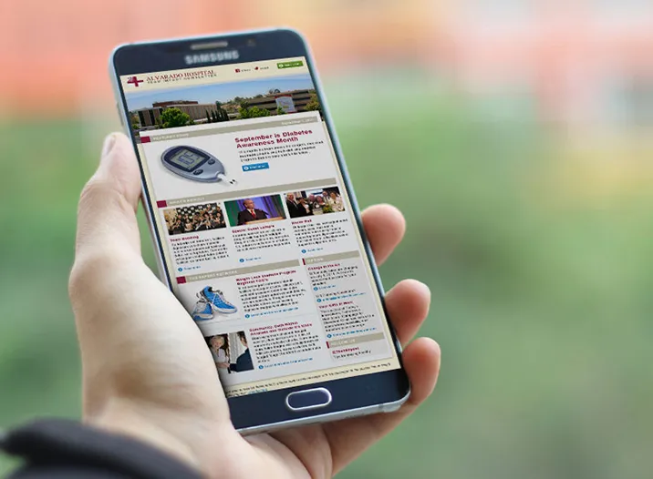 The Alvarado Hospital website shown on a phone held in one hand, with the hospital masthead, navigation, and a photo-led content column