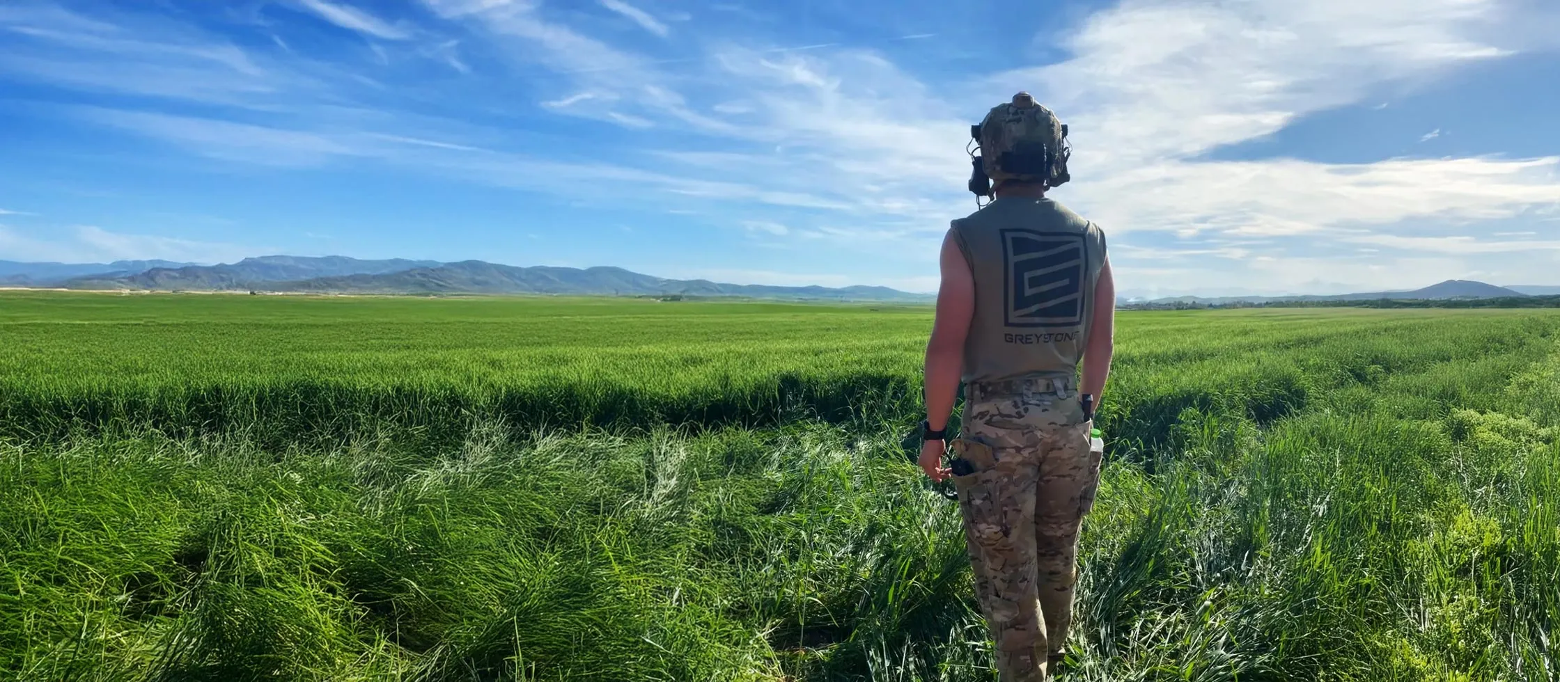 A person wearing a Greystone-branded shirt in an open field, the brand carried into the training environment