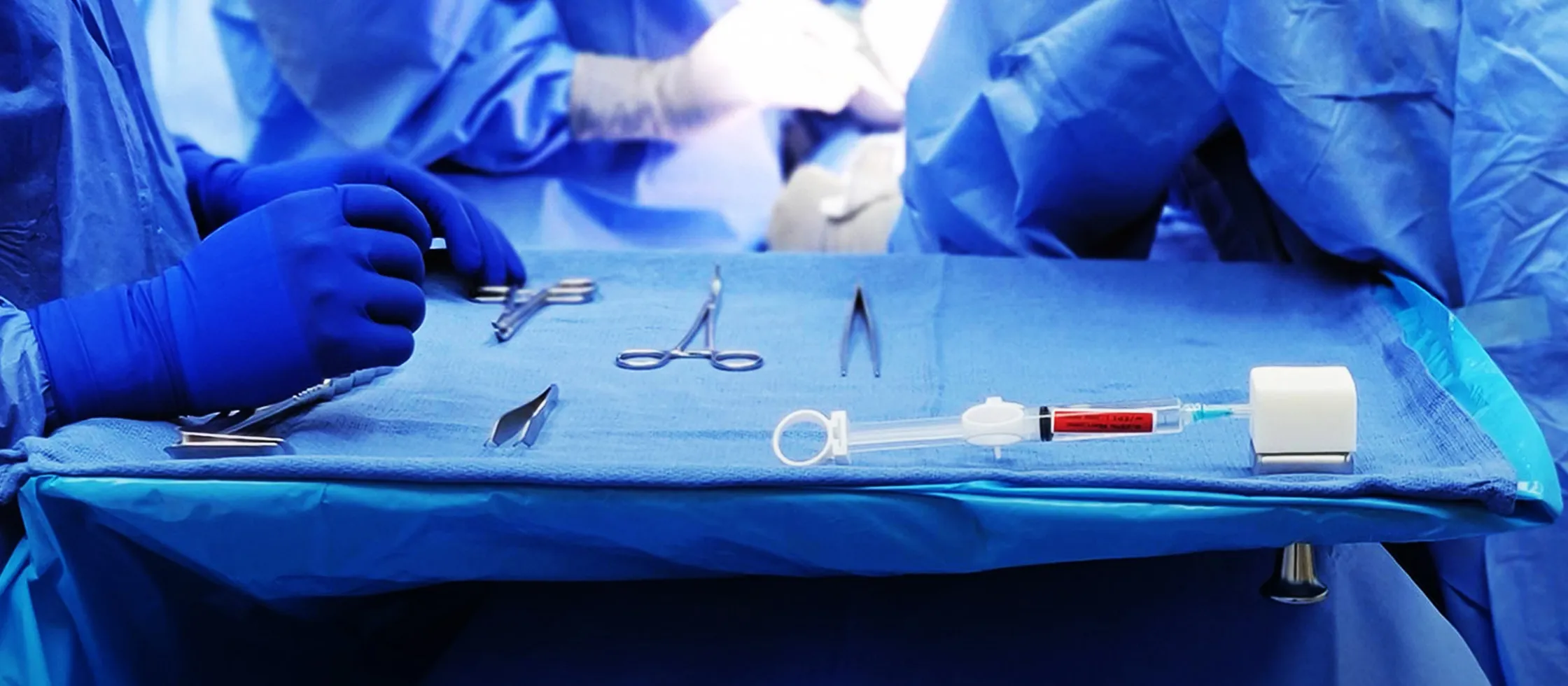 A draped surgical tray in an operating room: instruments laid out in a row, a filled syringe secured in the white HypoHolder block at the end of the tray