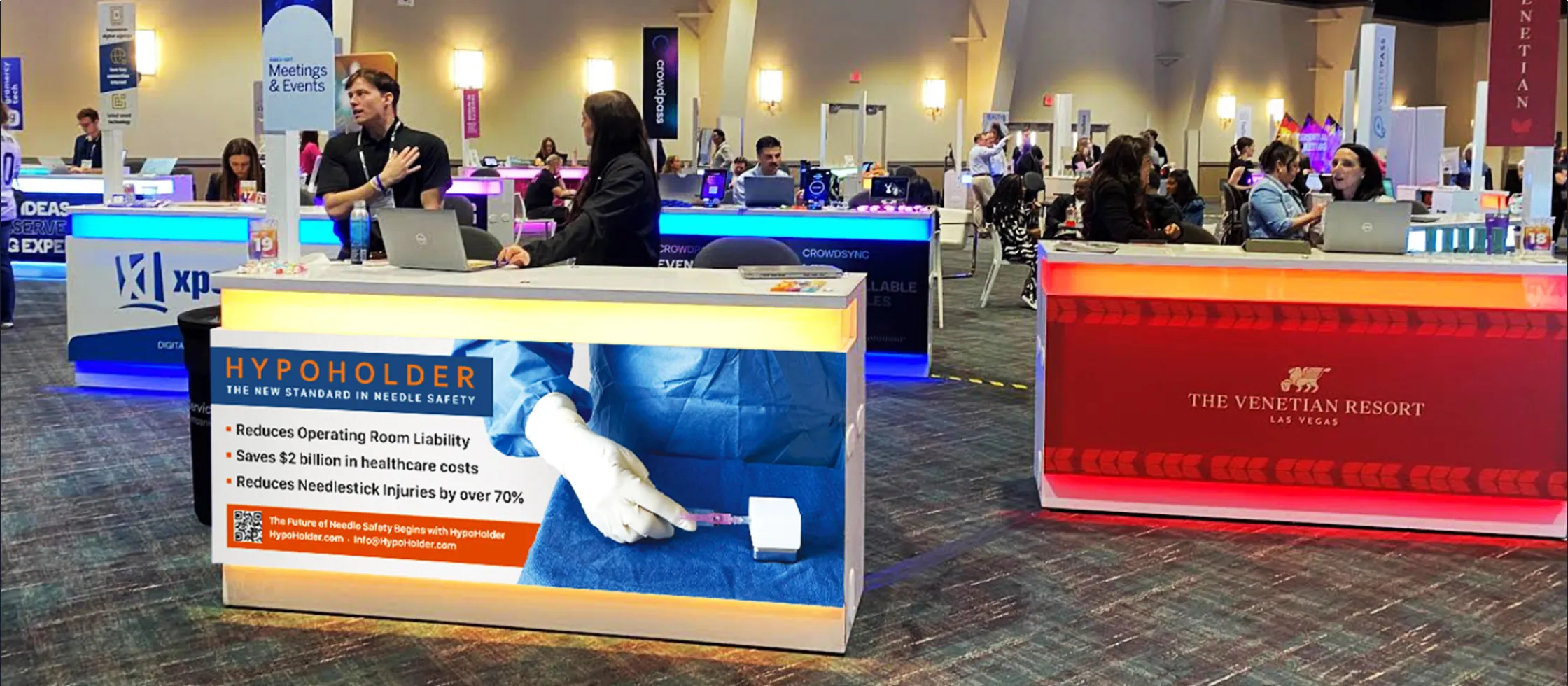 The lit HypoHolder counter on a trade-show floor, staffed and surrounded by other exhibitors