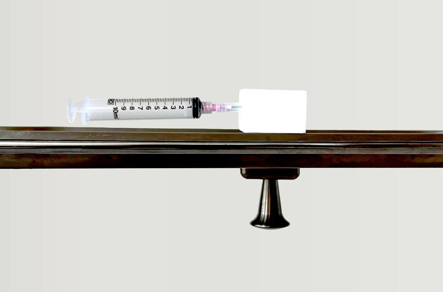 The HypoHolder mounted to the rail of a surgical stand, holding a capped hypodermic syringe clear of the work surface