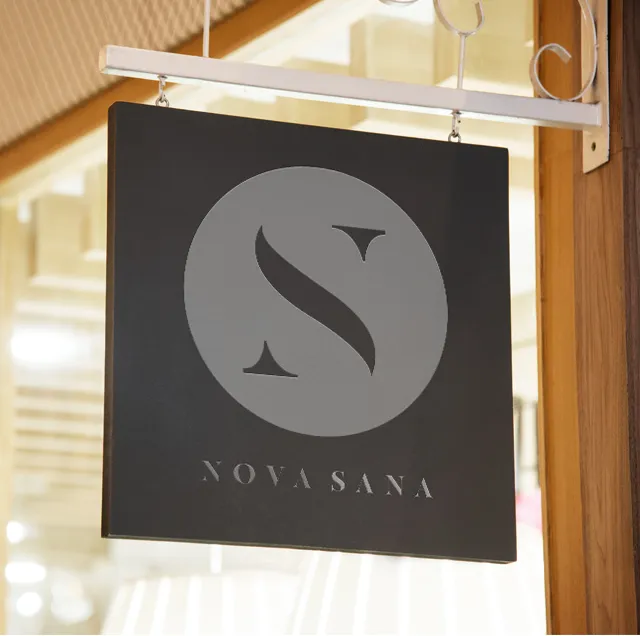 The Nova Sana hanging sign outside the entrance: the circular S mark and the name in white on a dark panel