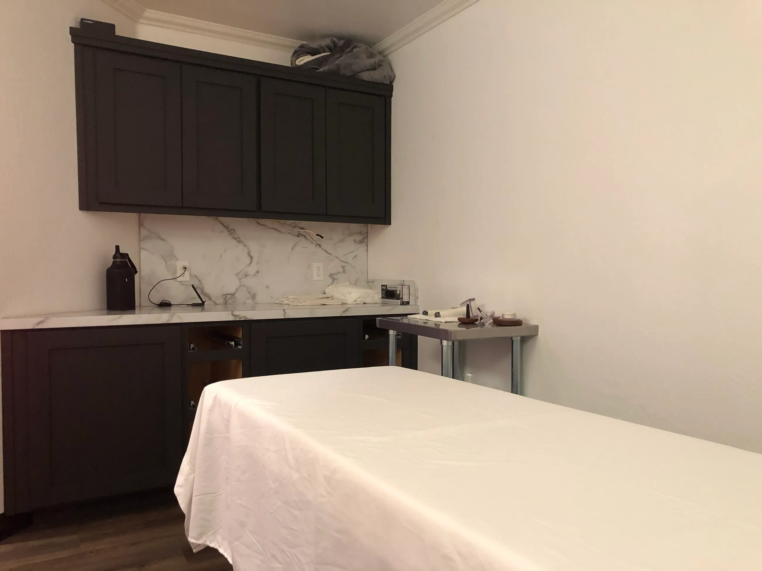 A Nova Sana treatment room: a made table, dark cabinetry and a marble counter